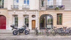 Un edificio con una puerta roja, una motocicleta estacionada adelante y varias bicicletas a lo largo de la acera.
