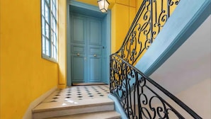 Una escalera con barandilla de hierro forjado negro, una puerta azul en la parte superior y una pared amarilla.