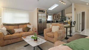 A compact living space with a sofa, armchair, and coffee table, a kitchenette with a refrigerator and microwave, and a door leading to another room. - Labernum (Preston)