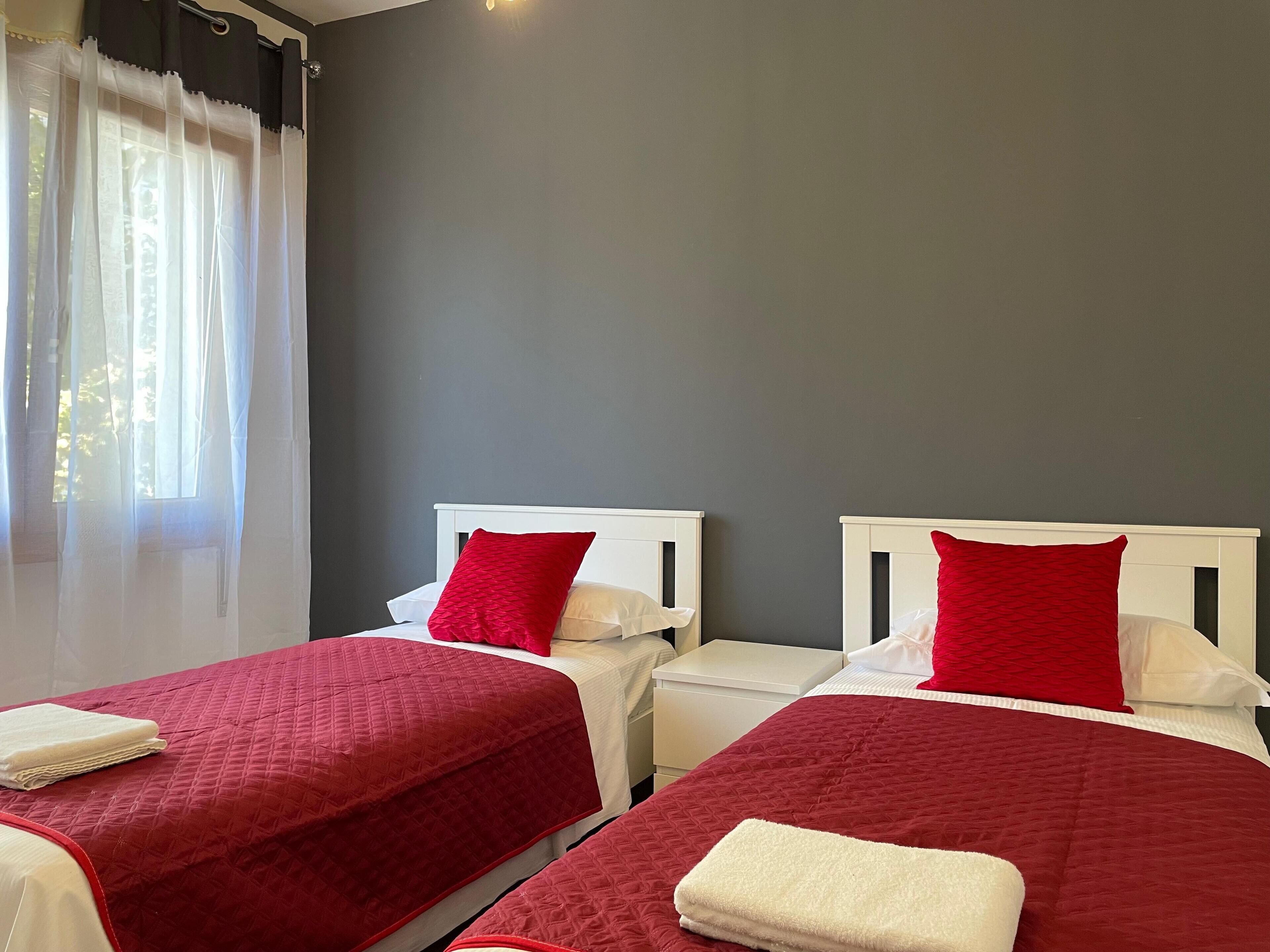 Une chambre d’hôtel avec deux lits, chacun recouvert d’une couverture rouge et doté d’une tête de lit blanche.
