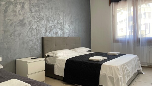 A bedroom with a bed, a nightstand, and a window with curtains. - Venetian Breeze (Mestre)
