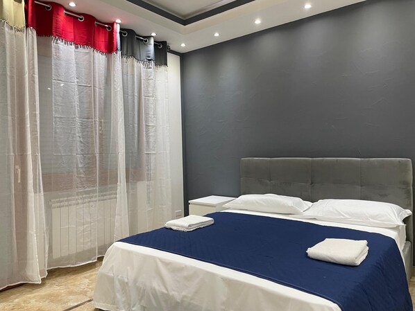 A bedroom with a bed, white curtains, and a grey headboard. - Venetian Breeze (Mestre)