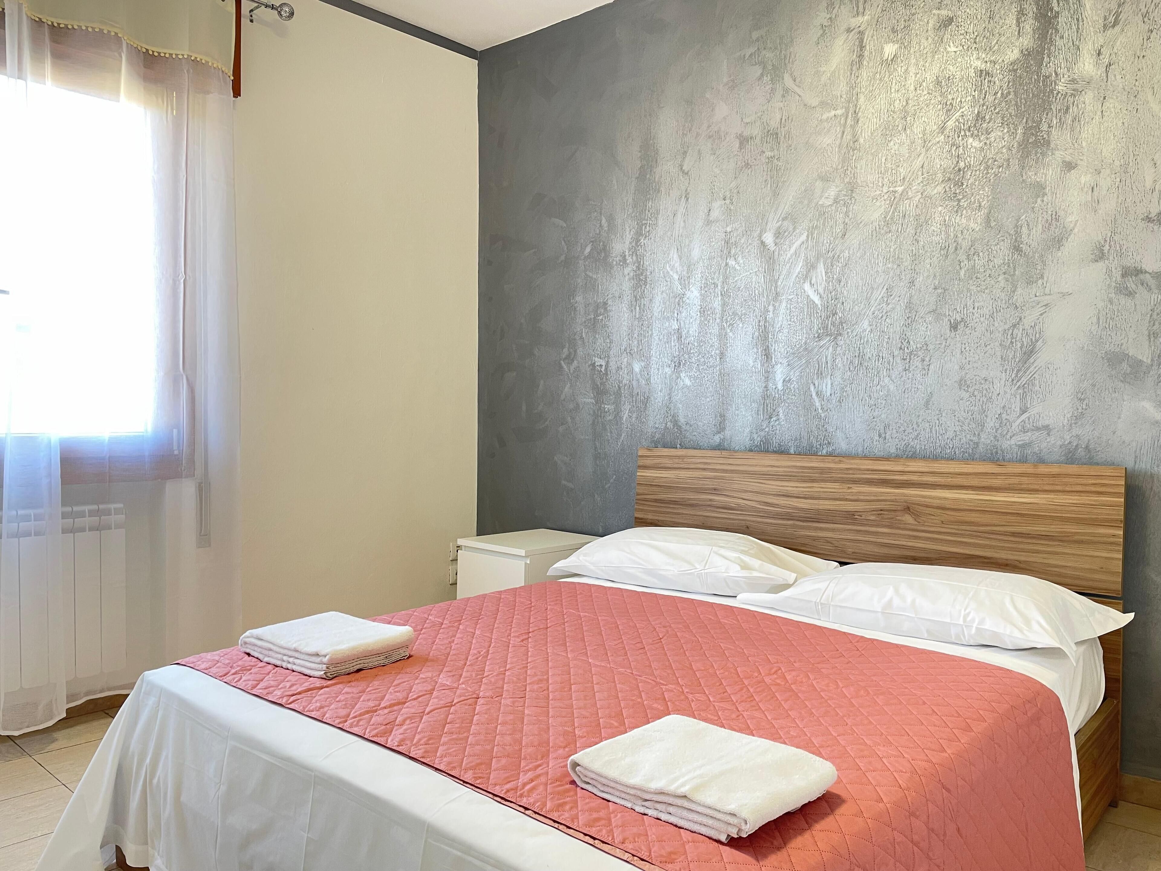 Cama bem arrumada com um edredom rosa, almofadas brancas e toalhas dobradas.