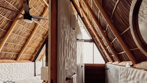 Une pièce avec un plafond en pente, des poutres en bois et une vue sur l’extérieur par une porte ouverte.