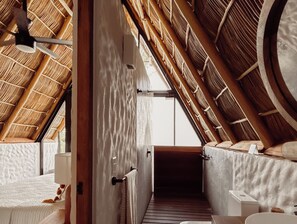 Une pièce avec un plafond en pente, des poutres en bois et une vue sur l’extérieur par une porte ouverte.