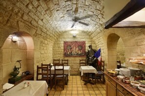 Un comedor con paredes de piedra, mesas y sillas, un ventilador de techo y suelo de baldosas.