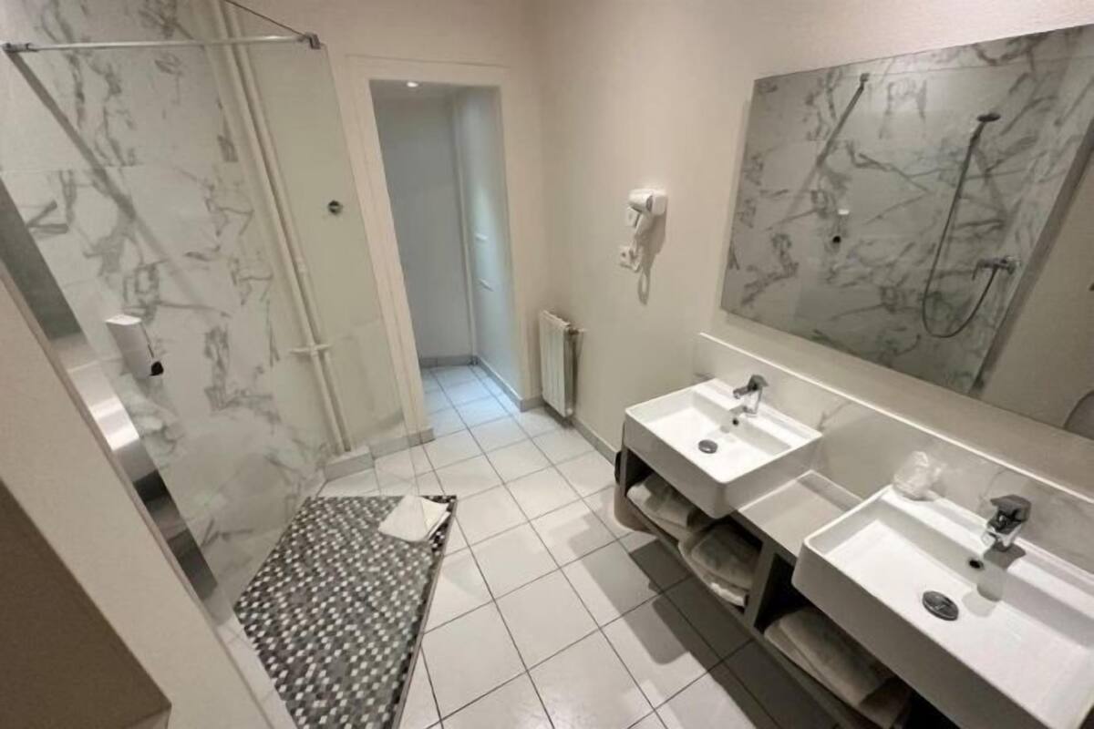 Un baño moderno con cabina de ducha de vidrio, dos lavamanos, un perchero para toallas y un salpicadero de mármol.