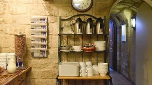 Un stretto corridoio in pietra con scaffali che espongono articoli da cucina e un orologio appeso al muro.