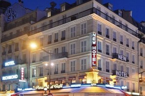 Un hotel con un llamativo letrero que dice 'NEW HOTEL', varios balcones y un bar en la planta baja llamado 'Paris N' Cafe'.