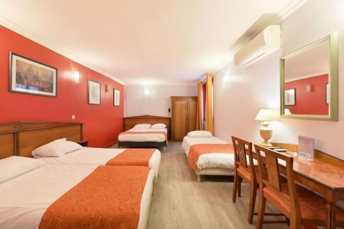 Una habitación de hotel con cuatro camas individuales, un escritorio de madera, una silla, un espejo y un cuadro en la pared.