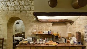 Cucina con pareti in pietra, un bancone in legno, diversi alimenti ed elettrodomestici.