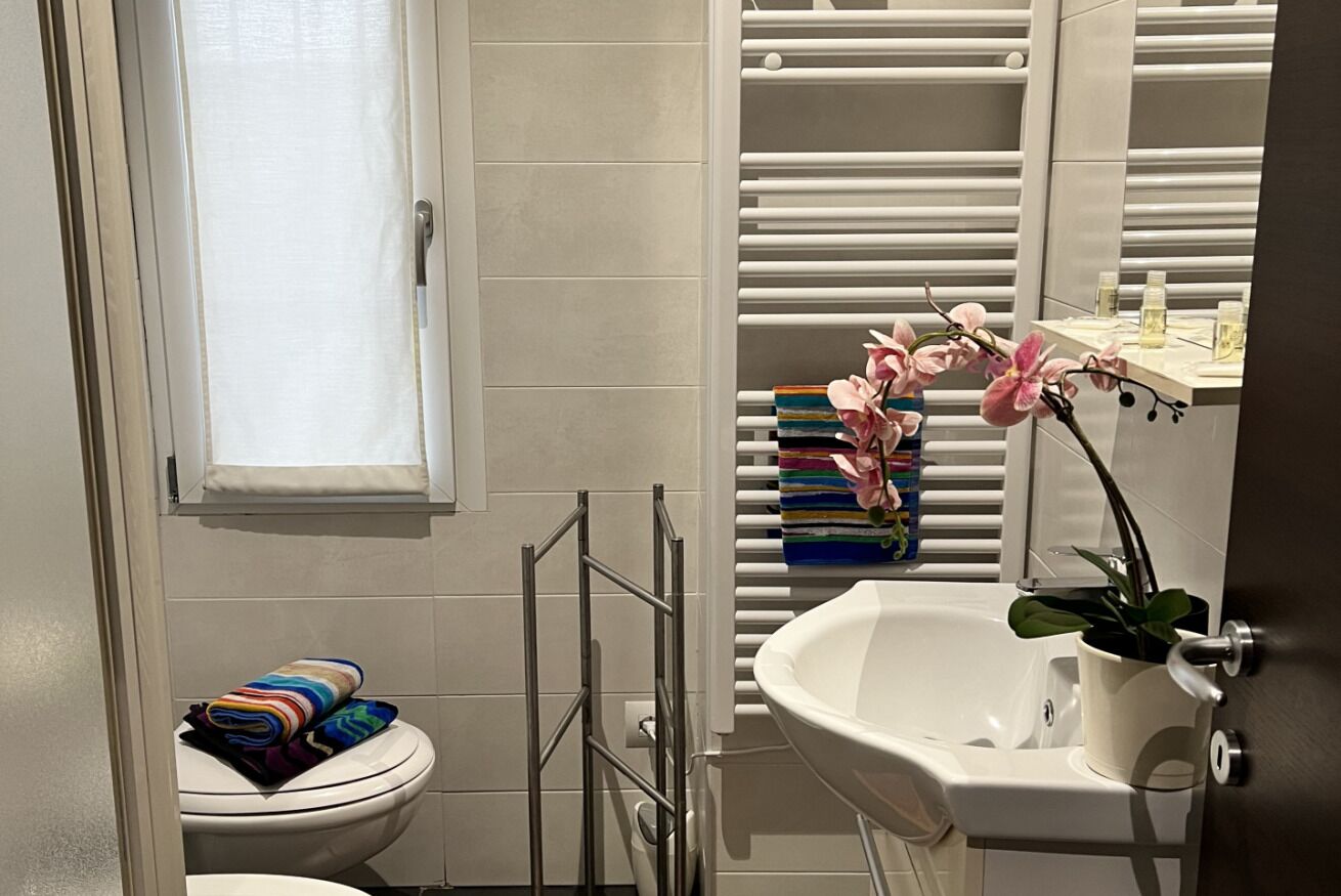 Un bagno con un water, un lavandino, un portasciugamani con asciugamani piegati e una finestra con una tenda bianca.