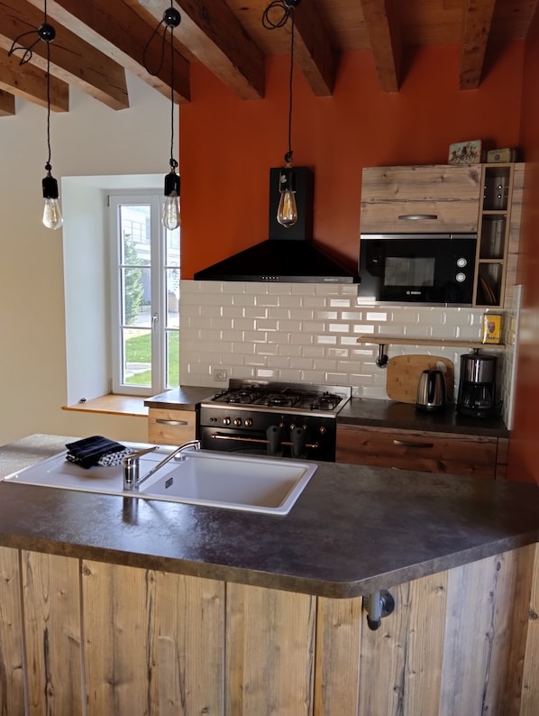 Una cocina con una isla central, horno Bosch, microondas y lámparas colgantes.