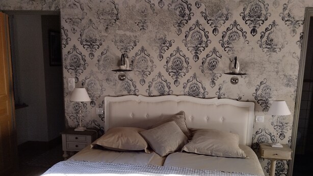 Un dormitorio con una cama grande, dos mesitas de noche, una lámpara en el techo y un papel pintado estampado.