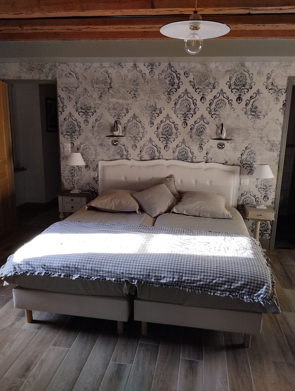 Une chambre à coucher avec un grand lit, deux tables de chevet, un luminaire au plafond et un papier peint à motifs.