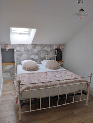 Un dormitorio con techo inclinado, cama con colcha estampada, dos lámparas de noche y un tragaluz.