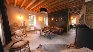 Una sala de estar acogedora con vigas de madera, un sofá de cuero, sillas de mimbre y una chimenea.