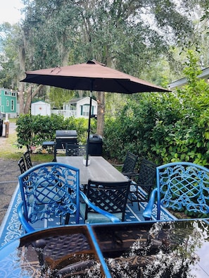 Eine Terrasse im Freien mit Tisch, Stühlen, einem Grill und einem Sonnenschirm.