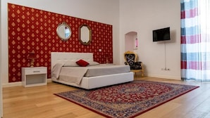 A bedroom with a bed, a nightstand, a mirror, a TV, and a patterned rug. - Palazzo delle Puglie B&B (Barletta)