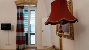 A room with a red lamp, a television, a door with striped curtains, and a framed picture on the wall. - Palazzo delle Puglie B&B (Barletta)