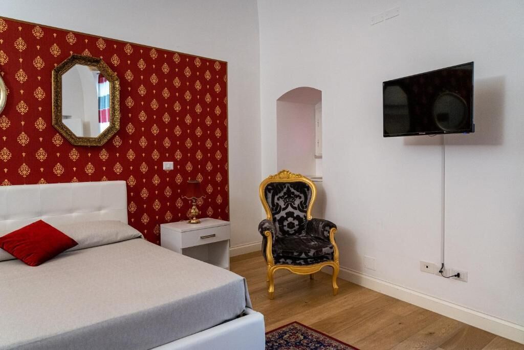 Un dormitorio con cama, televisor, espejo y una silla.