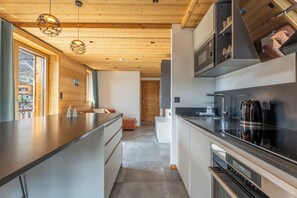 A modern kitchen with wooden ceiling, built-in appliances, and pendant lighting.