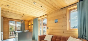 A wooden cabin interior with a dining area, a sofa, and a view of the outside.