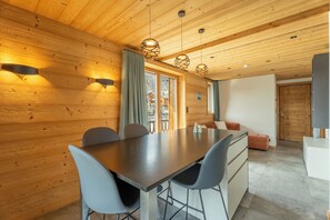 A wooden interior with a dining table, chairs, pendant lights, and a view through a window. - Apartment Gondola (Les Gets)