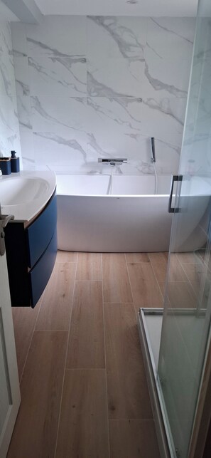 Ein modernes Badezimmer mit einer weißen Badewanne, einer Duschkabine aus Glas und einem Holzboden.