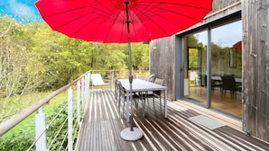 A wooden deck with a red umbrella, a table, and chairs. - Loft Ôvebas at Domaine De L'ô (Eyraud-Crempse-Maurens)