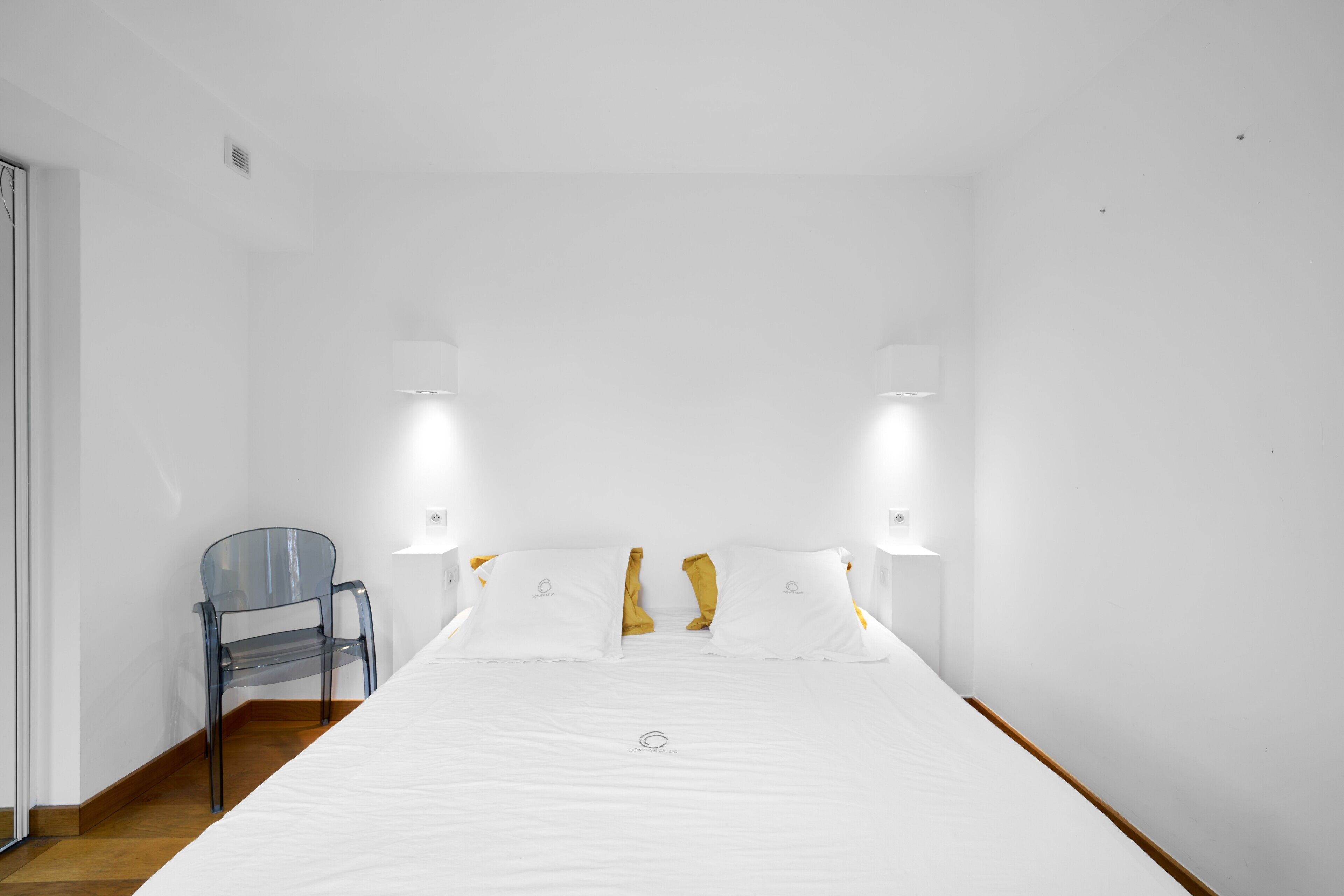 A hotel room with a large bed, a chair, and two wall-mounted lights.
