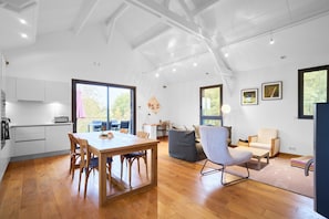 Een ruime woonkamer met een houten eettafel, een grijze fauteuil en een bank.