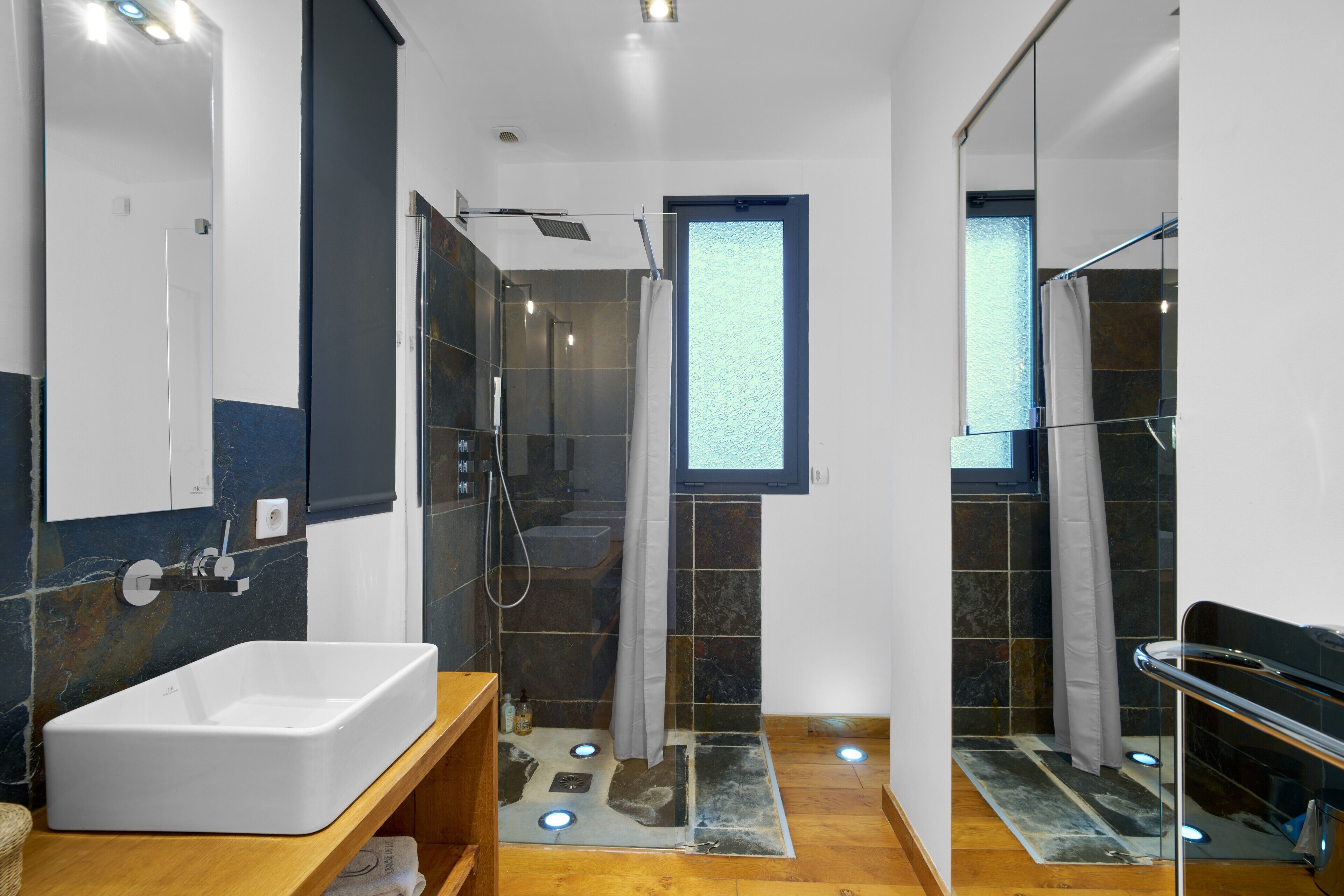 A modern bathroom with a large white sink, a glass shower enclosure, and a small window.