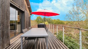 Une terrasse en bois avec une table et des chaises, un parasol rouge et une vue sur le paysage environnant.