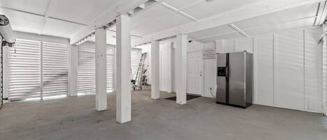 A spacious, industrial-style room with white walls and ceiling, featuring a stainless steel refrigerator and a ladder leaning against the wall.
