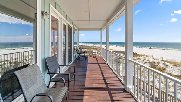 A covered porch with a view of the beach, featuring a wooden deck, chairs, and a railing. - Seanile (Orange Beach)