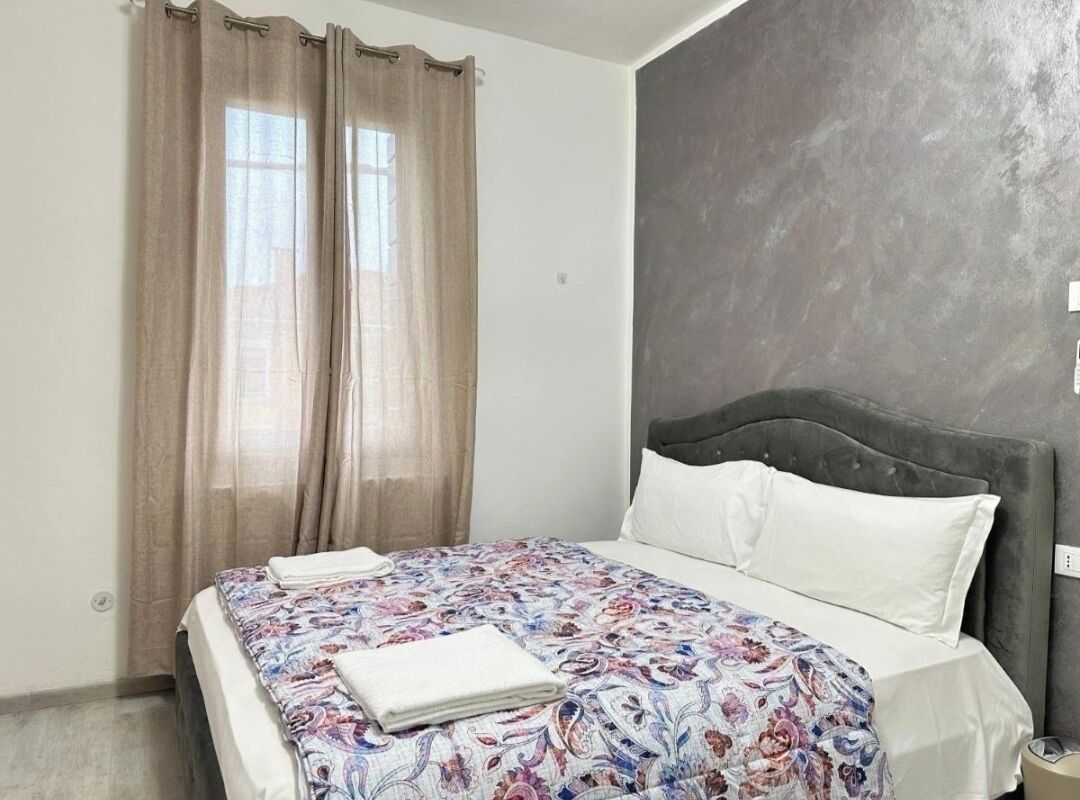 A bedroom with a bed, curtains, a headboard, and a plain wall.