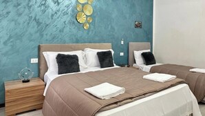 A modern bedroom with two beds, a teal accent wall, and decorative wall art. - Venetian Nexus (Mestre)