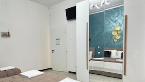 A hotel room with a large bed, a mirror, a television, and a teal-colored wall with decorative plates. - Venetian Nexus (Mestre)