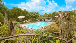 Une piscine dotée d’une terrasse en bois, entourée de verdure et d’arbres.