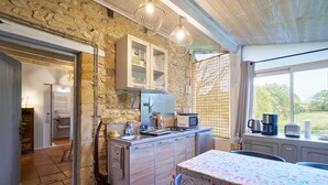 Une cuisine avec un mur en pierre, des armoires en bois, un sol carrelé et un coin repas comprenant une table et des chaises.