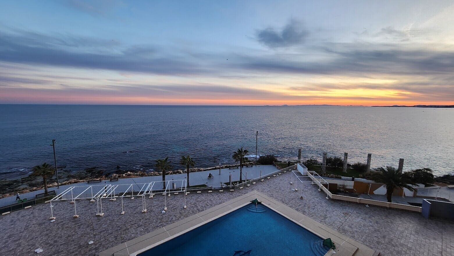 A pool area with a view of the sea and a sunset.