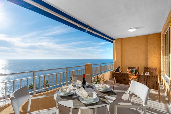 A balcony with a table set for dining, overlooking the sea.