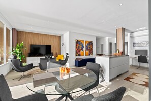 A modern living room with a glass dining table, black chairs, a TV, and artwork on the walls.