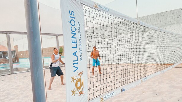 A beach volleyball court with a net, sand, and a building in the background. - Pousada Vila Lençóis e Sport (Barreirinhas)