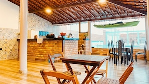 An indoor dining area with wooden tables and chairs, a brick wall, and a view of a green boat outside. - Pousada Vila Lençóis e Sport (Barreirinhas)
