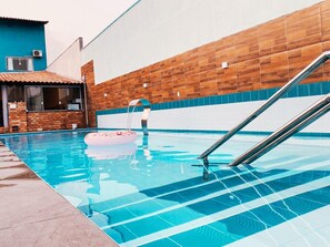 Una piscina amb una paret de fusta, un edifici de maó i una escala metàl·lica.