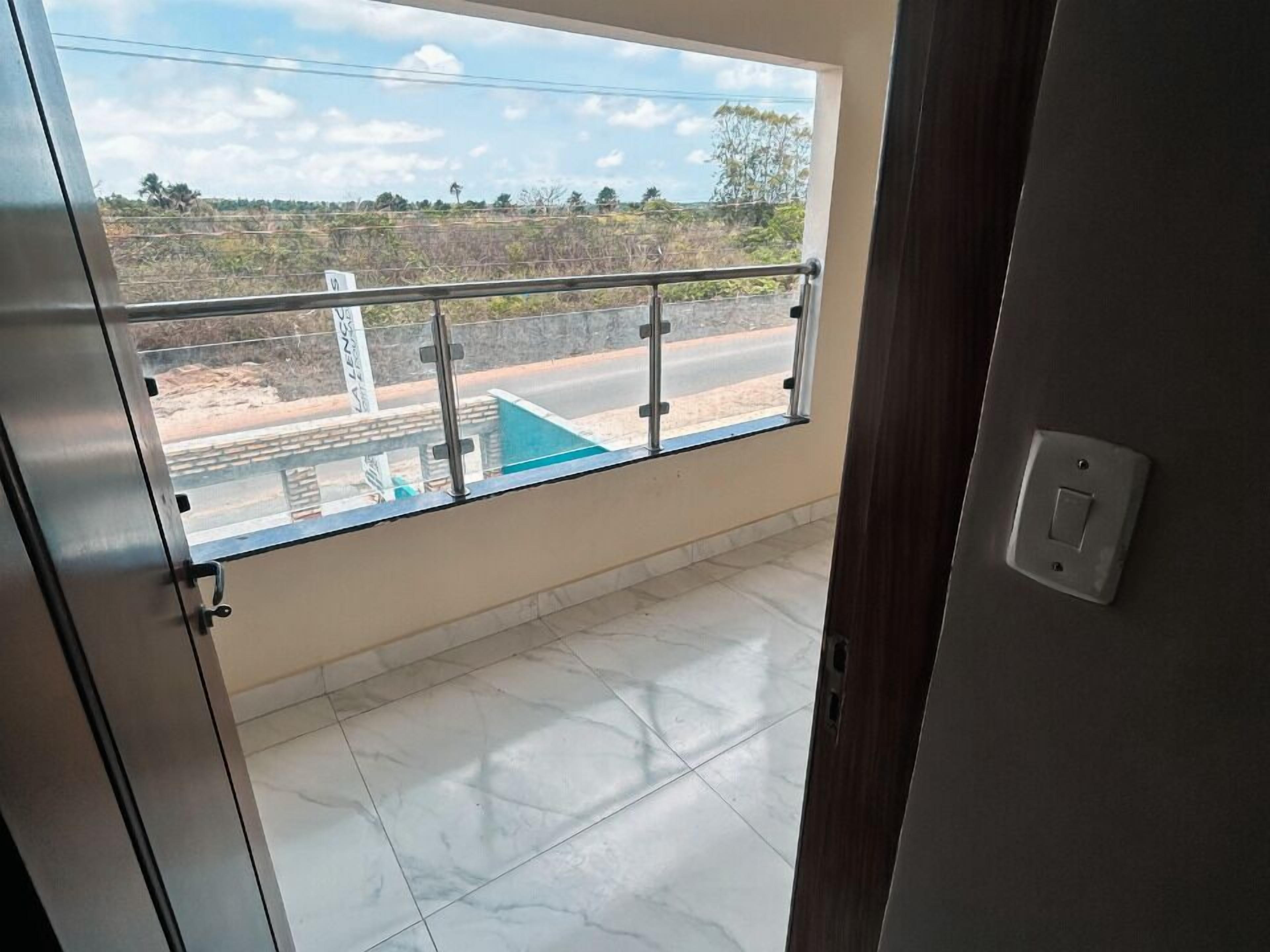 A room with a large window, a balcony with a metal railing, and a tiled floor.