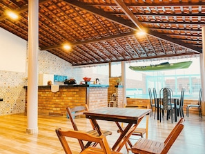 Un comedor interior con pared de ladrillo, techo de madera y piscina visible a través de la ventana.