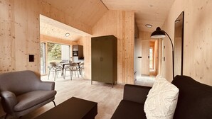 Un interior moderno con techo de madera, zona de comedor con mesa y sillas, sofá con cojín blanco y un armario.